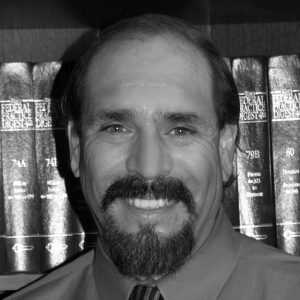 Black and white photo of Dan Marco, a man with a dark mustache and a beard