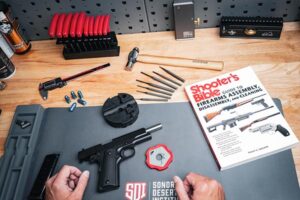 Disassembled handgun, tools, and a copy of the Shooter’s Bible laid out on a Sonoran Desert Institute workbench during firearm maintenance training.