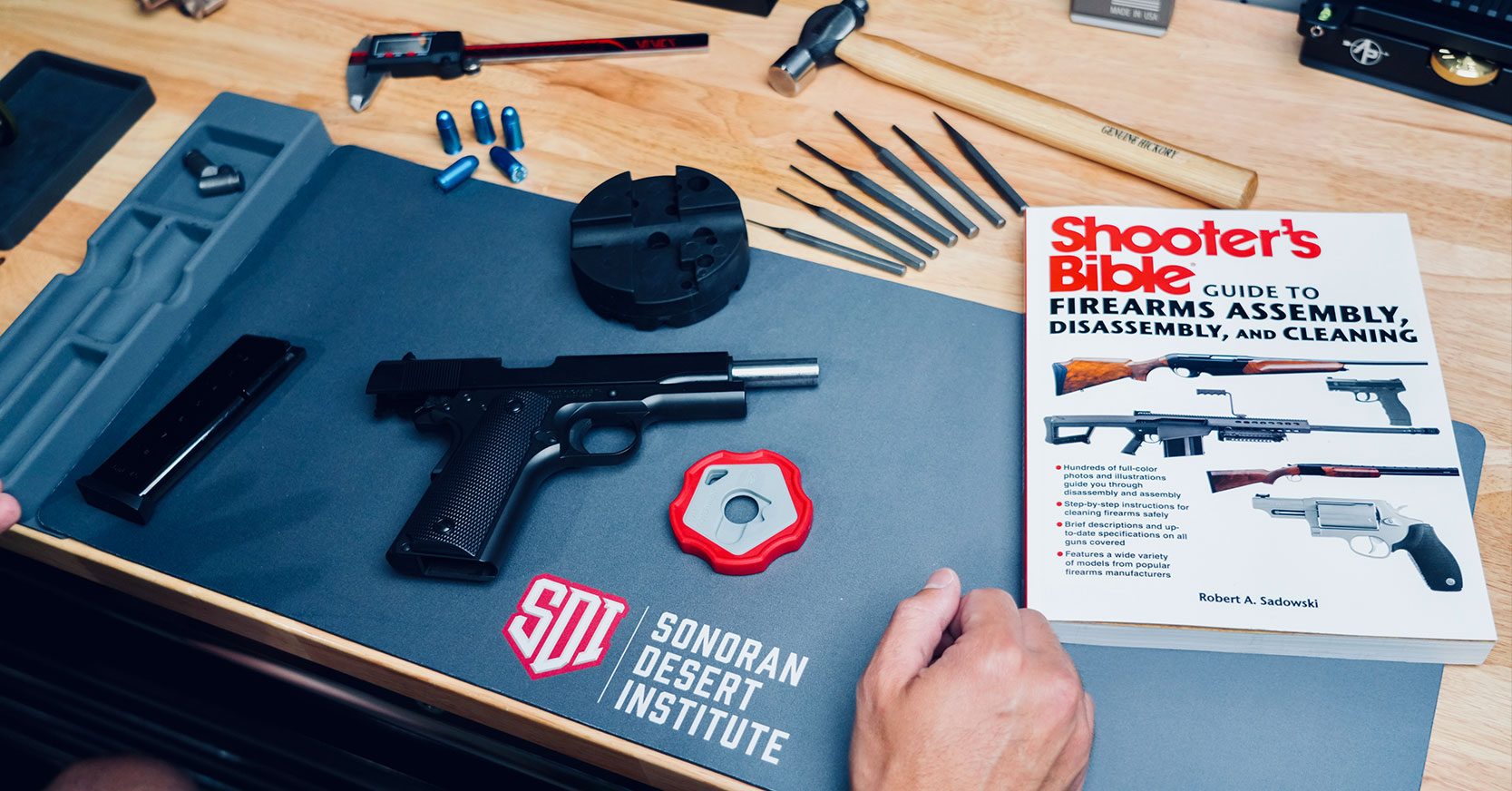 Firearm cleaning setup on SDI mat with tools, parts, and Shooter’s Bible manual
