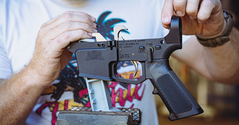 Man assembling a Palmetto State Armory AR lower receiver using a vise in a home workshop.