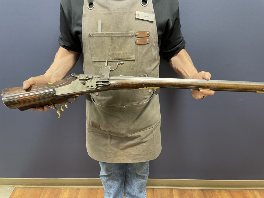 Bart Miller, SDI's gunsmithing instructor, holding a restored wheellock rifle with its ornate lock mechanism and brass fittings visible.